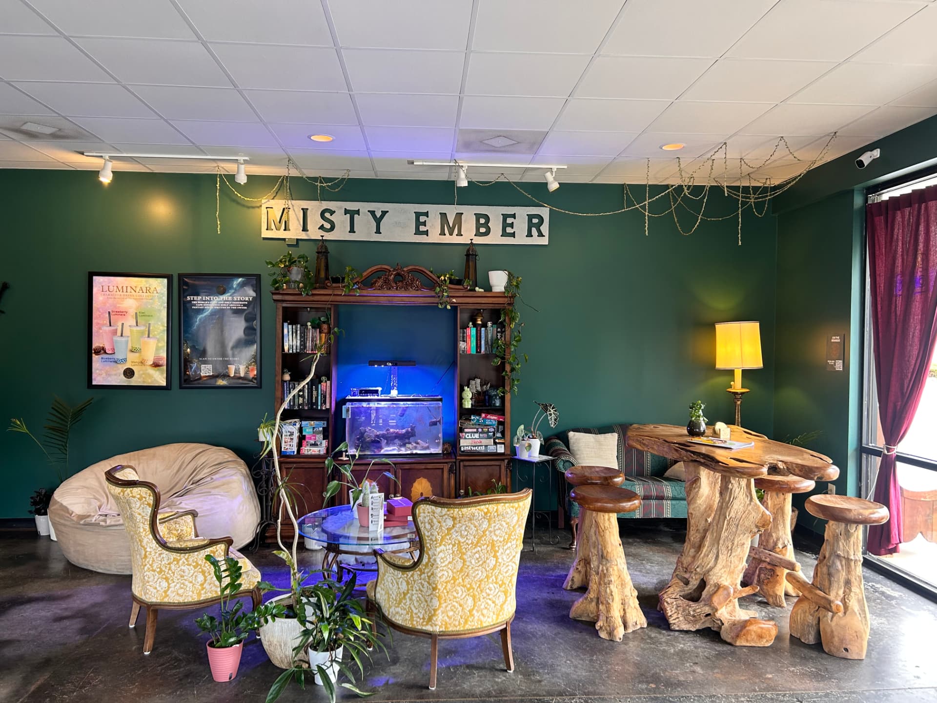 The Misty Ember Café lounge: yellow armchairs around a glass table, a carved wooden hutch with a lit aquarium, and the Misty Ember wall sign