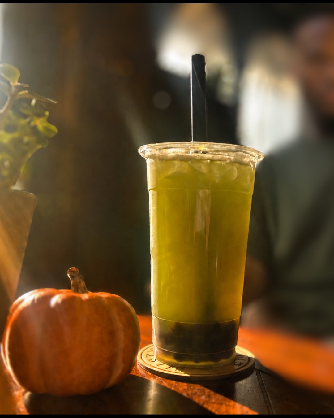 Green tea with pearls beside a small pumpkin in warm café light